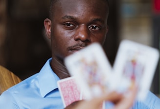 A person wearing a blue shirt is focused intently on playing cards held by someone else. The image highlights a mix of concentration and strategic thinking in a casual setting.