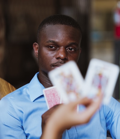 A person wearing a blue shirt is focused intently on playing cards held by someone else. The image highlights a mix of concentration and strategic thinking in a casual setting.