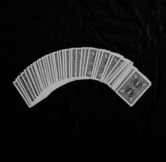 A neatly arranged spread of playing cards with an intricate design on their backs, set against a dark fabric background. The cards form a gentle curve, creating a sense of symmetry and order.