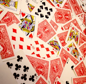 A vibrant assortment of playing cards scattered in a chaotic manner. The cards display various suits and numbers, predominantly featuring the colors red and black with intricate designs. Several face cards are visible, showcasing traditional royal characters in vivid detail.