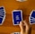A hand holds a playing card with Arabic text printed on it. Several other cards are spread out on a wooden surface in different positions.