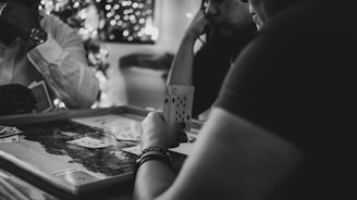 Three people are engaged in a card game, sitting around a table in a cozy, dimly lit setting. One player is holding an Ace and a Ten of diamonds. There are fairy lights and a blurred Christmas tree in the background, adding a festive and warm atmosphere to the scene.